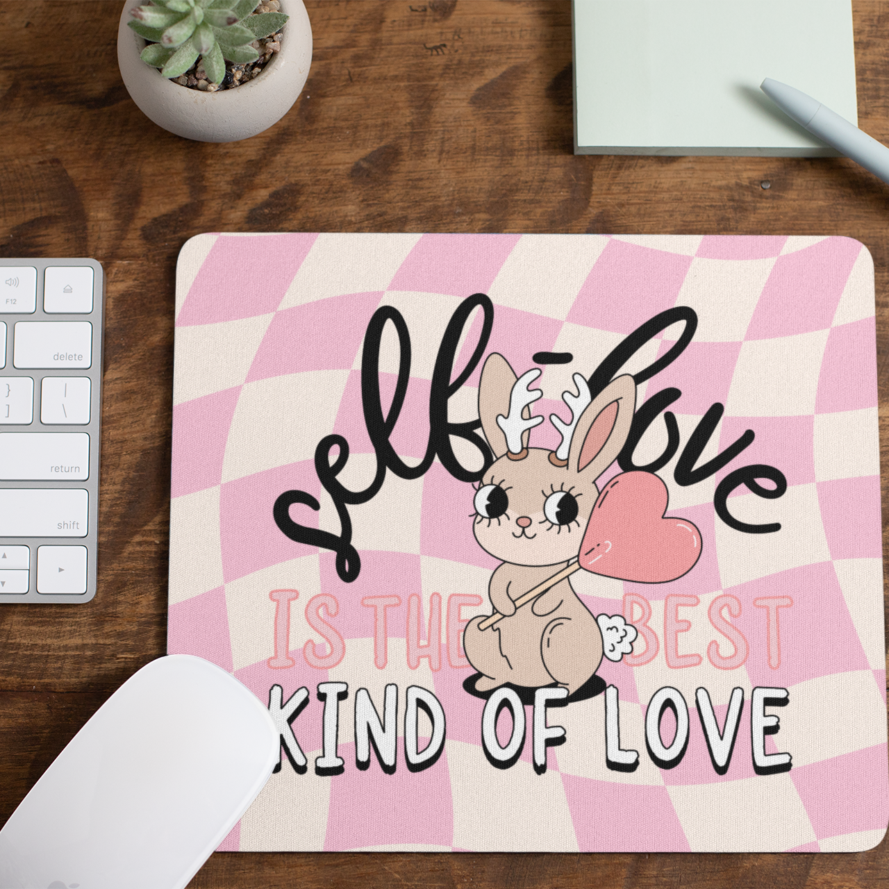 Mouse pad with a bunny illustration and text on a wooden desk with a keyboard and pen.