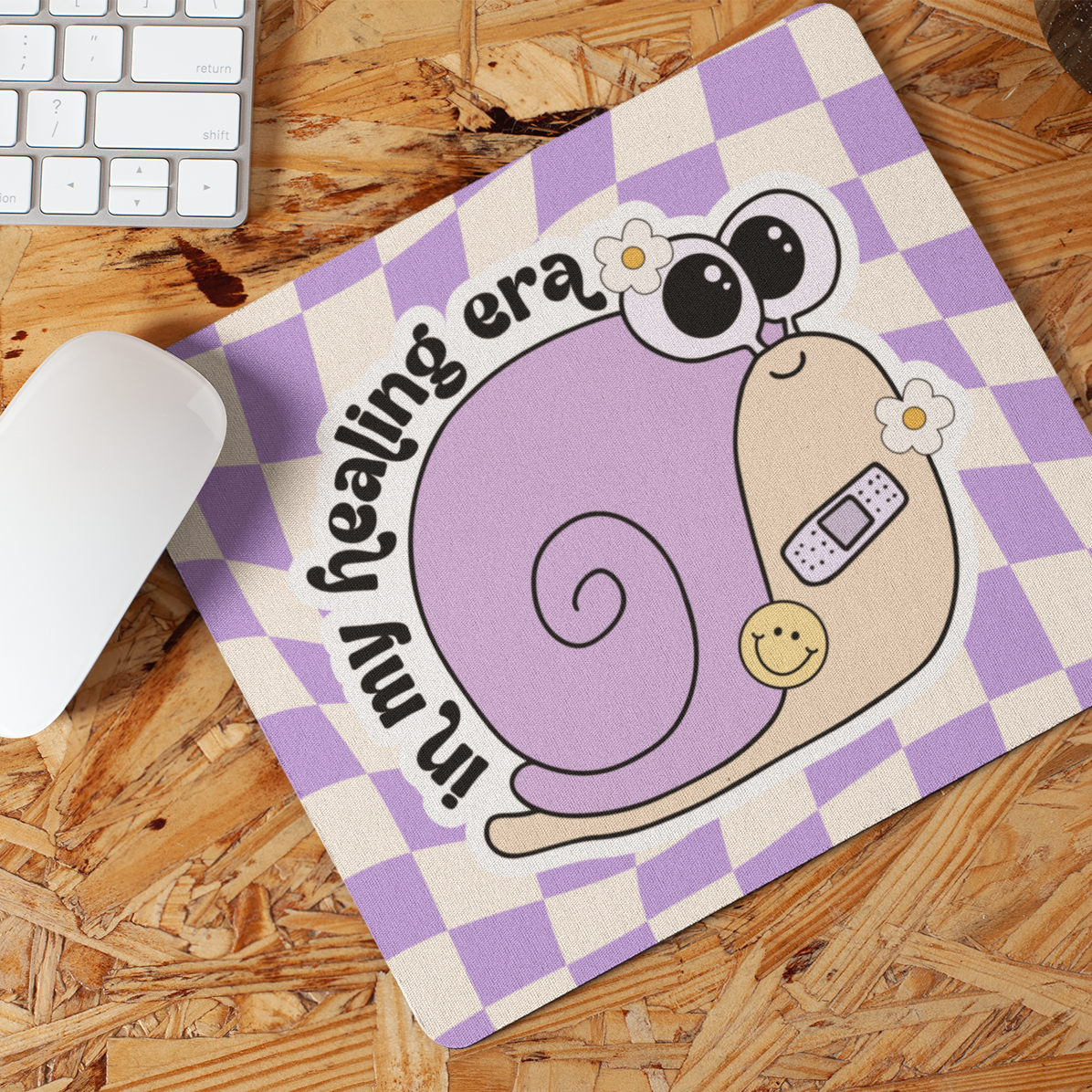 Mouse pad with a snail design and text on a wooden desk with a keyboard and mouse.