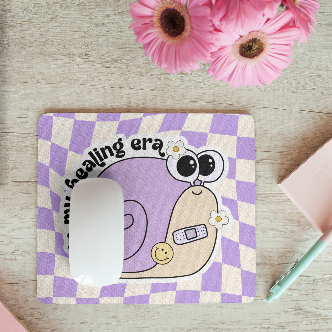 Checkered mouse pad with cartoon character on a desk with laptop and flowers